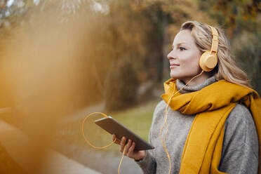 Woman listening music through headphones during autumn - JOSEF05376