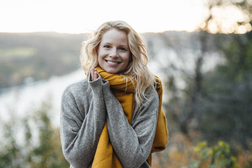 Blond woman in gray sweater smiling during sunset - JOSEF05378