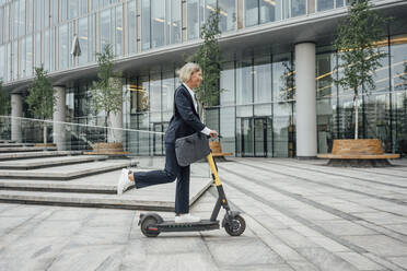 Geschäftsfrau fährt im Büropark mit einem Elektroroller - VPIF04459