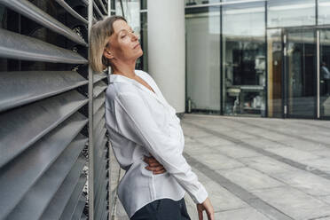 Female professional contemplating while leaning on blinds at office park - VPIF04464