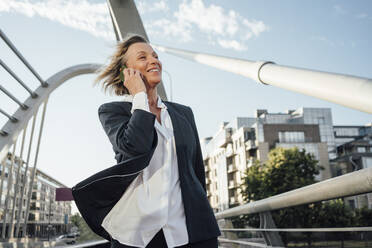 Mature businesswoman looking away while talking on smart phone in city - VPIF04495