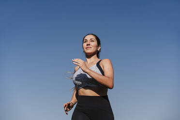 Junge entschlossene Sportlerin joggt bei Sonnenuntergang - EBBF04506