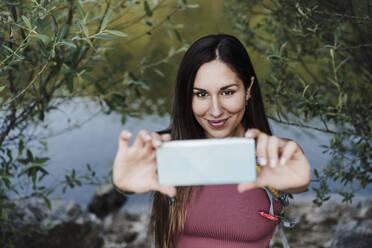 Schöne junge Frau nimmt Selfie durch Handy am Seeufer - EBBF04522