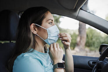 Young woman wearing protective face mask in car during COVID-19 - EBBF04545