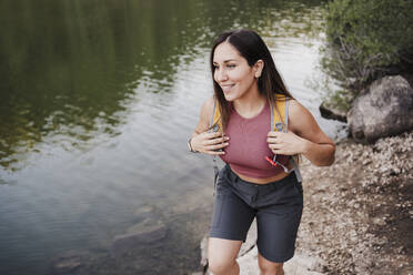 Smiling female hiker walking at lakeshore - EBBF04557