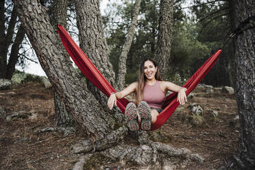 Smiling young woman swinging on hammock in forest - EBBF04569