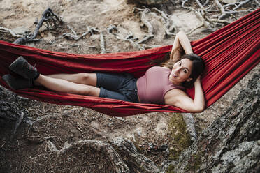 Smiling young woman with hands behind head relaxing on hammock - EBBF04577