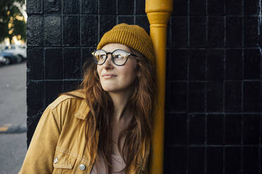 Young woman wearing knit hat contemplating while leaning on pipe - VPIF04528