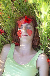 Girl with petals on face relaxing at poppy field - BFRF02360