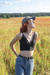 Teenage girl with cap standing in poppy field - BFRF02365