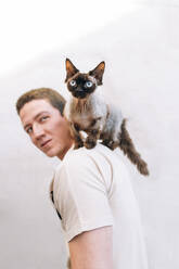 Man looking at cat on shoulder by wall - EGHF00146
