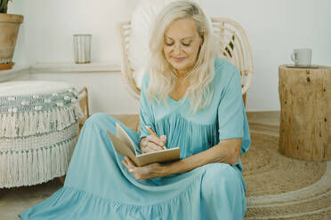 Woman writing in book while sitting at home - ERRF04940