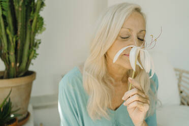 Senior woman smelling white flower at home - ERRF04946