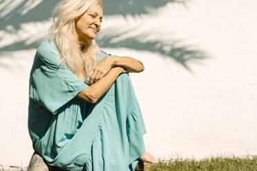 Lächelnde Frau, die in einem sonnigen Tag im Hinterhof sitzt und nachdenkt - ERRF04959