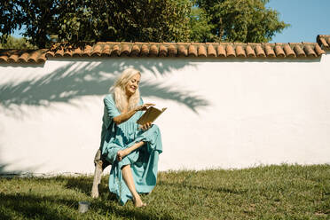 Frau liest ein Buch, während sie an einem sonnigen Tag im Hinterhof sitzt - ERRF04962