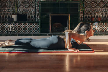 Junge Frau übt Yoga, während sie zu Hause auf einer Übungsmatte liegt - MRRF01290