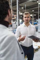 Geschäftsmann hält ein digitales Tablet in der Hand, während er sich mit einem Kollegen in einer Fabrik unterhält - DIGF16149