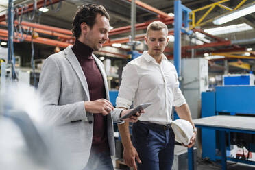 Businessman using digital tablet while walking by male colleague at factory - DIGF16155