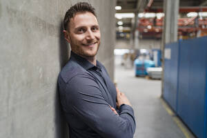 Smiling male professional with arms crossed leaning on gray wall - DIGF16176