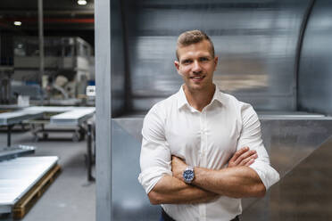 Smiling young male professional with arms crossed at factory - DIGF16181