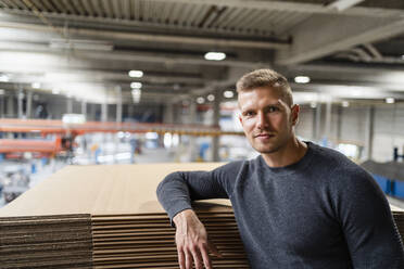 Young businessman staring while leaning on cardboard stack - DIGF16209