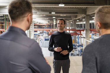 Smiling male professional having discussion with colleague at industry - DIGF16216