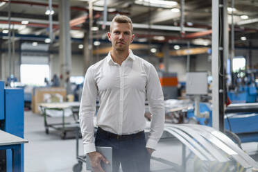 Selbstbewusster junger Geschäftsmann, der mit der Hand in der Tasche ein digitales Tablet in einer Fabrik hält - DIGF16242