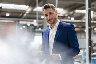 Geschäftsmann mit blauem Blazer, der ein digitales Tablet in der Industrie hält - DIGF16244