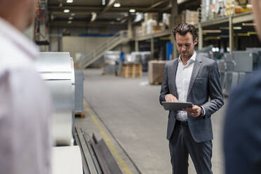 Businessman using digital tablet while standing near colleagues in factory - DIGF16280