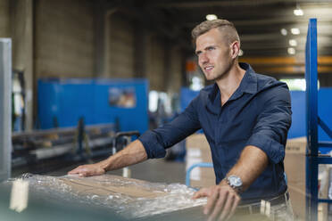 Thoughtful young male professional standing by cardboard box in industry - DIGF16295