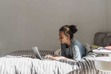 Frau benutzt Laptop, während sie zu Hause auf dem Bett liegt - MEUF03720