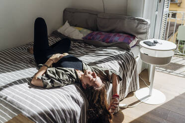 Gelangweilte Frau mit langen braunen Haaren auf dem Bett liegend in einer Wohnung - MEUF03741