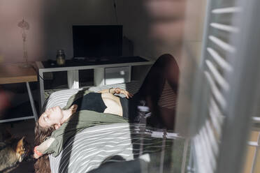 Frau entspannt auf dem Bett liegend durch ein Fenster gesehen - MEUF03742