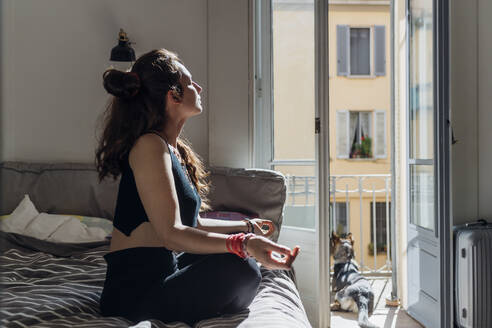 Frau meditiert beim Yoga auf dem Bett in der Wohnung - MEUF03747