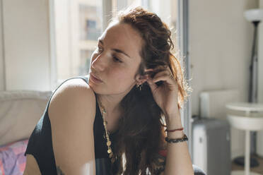 Thoughtful woman with hand in hair looking away at home - MEUF03752