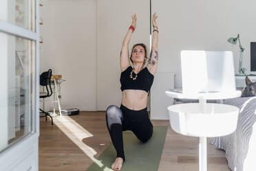 Woman with hands raised stretching on exercise mat at home - MEUF03767