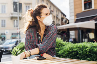 Woman wearing protective face mask while sitting at sidewalk cafe during pandemic - MEUF03773