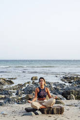 Woman doing lotus position on rock at beach - PGF00714