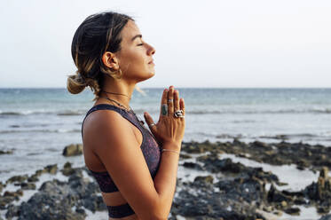 Young woman with hands clasped meditating at beach - PGF00717