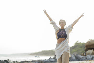 Carefree woman with arms raised walking at beach - PGF00733