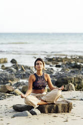 Junge Frau übt Yoga auf einem Felsen am Strand - PGF00738