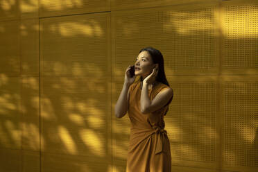 Young woman talking on smart phone in front of yellow wall - EAF00035