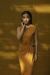 Beautiful young woman wearing orange dress standing in front of yellow wall - EAF00039