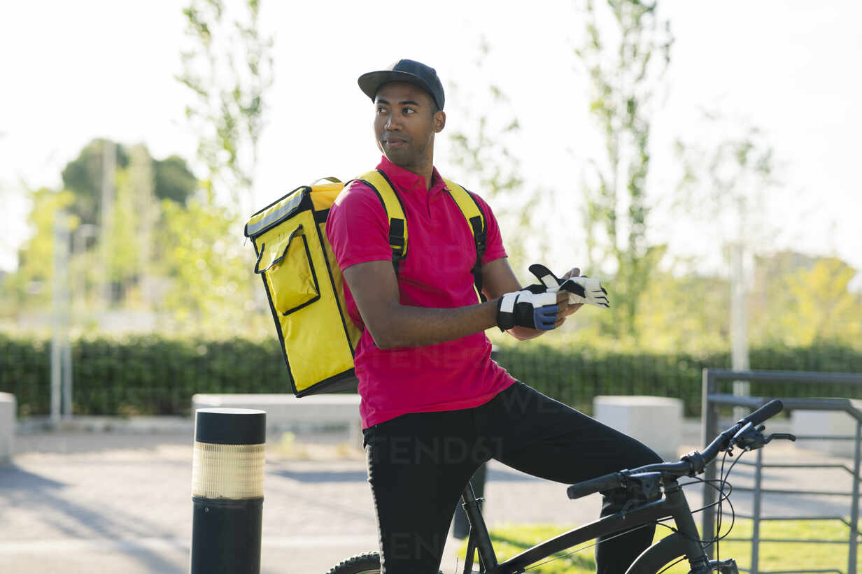 https://us.images.westend61.de/0001595744pw/delivery-man-with-gloves-looking-away-while-sitting-on-bicycle-JCCMF03480.jpg