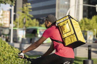 Zusteller mit gelbem Rucksack auf dem Fahrrad an einem sonnigen Tag - JCCMF03481