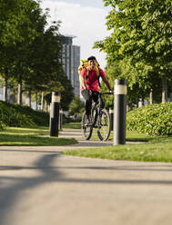 Lächelnder Zusteller auf dem Fahrrad im Park an einem sonnigen Tag - JCCMF03482