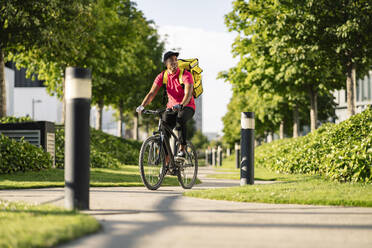 Männlicher Zusteller, der beim Fahrradfahren im Park wegschaut - JCCMF03483