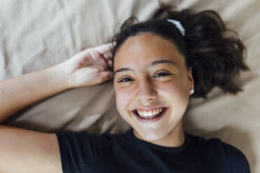 Happy girl with hand in hair on bed - EGHF00165
