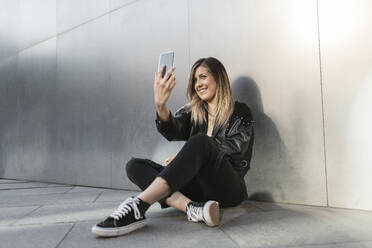 Frau, die ein Selfie mit ihrem Smartphone vor einer Metallwand macht - MTBF01069