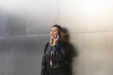 Young woman talking on smart phone in front of silver wall - MTBF01073